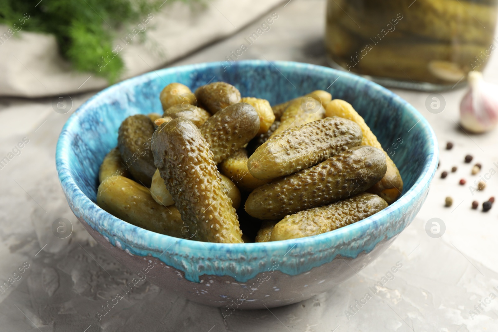 Photo of Pickled cucumbers in bowl on grey textured table, closeup