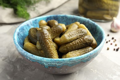 Pickled cucumbers in bowl on grey textured table, closeup