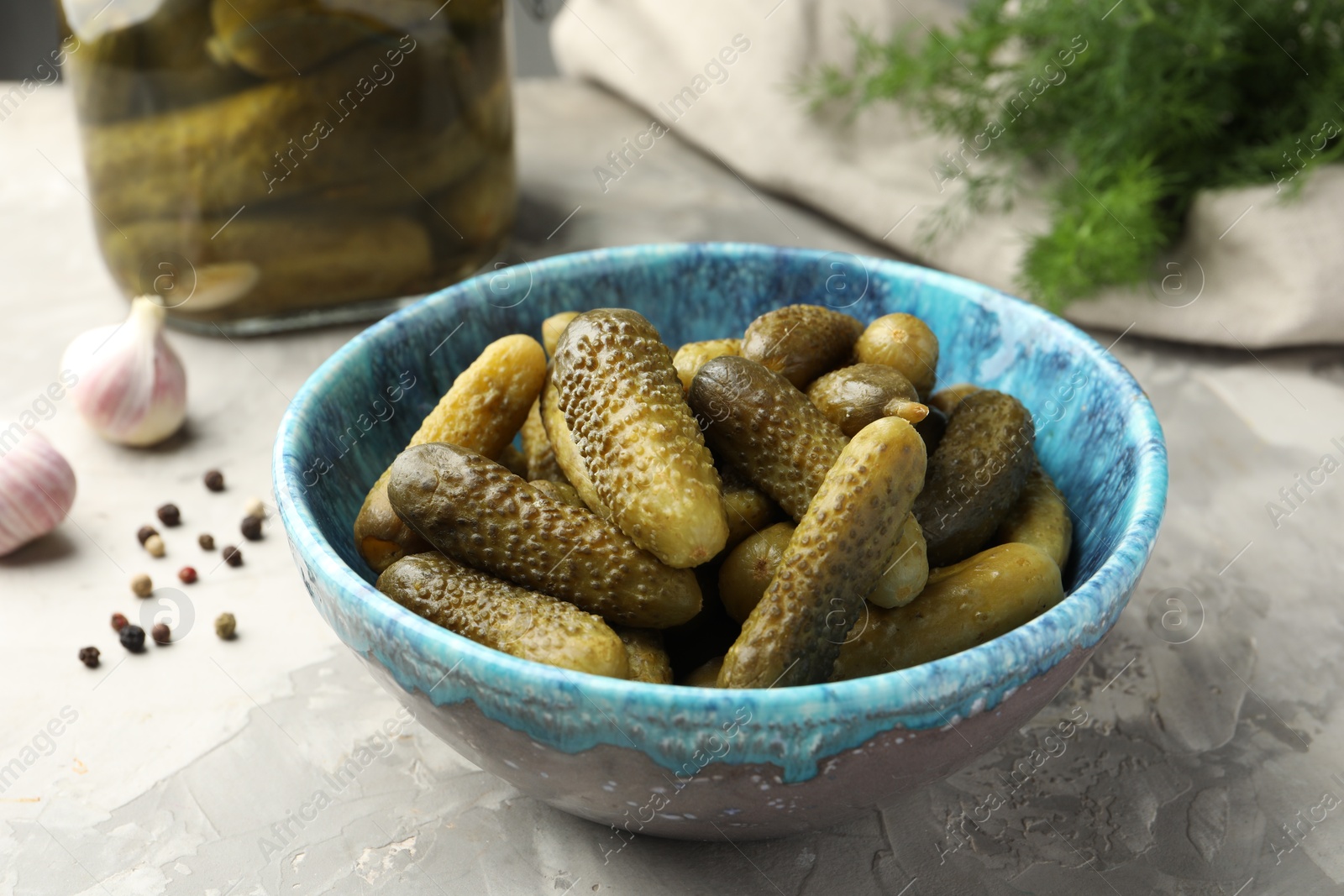 Photo of Pickled cucumbers in bowl on grey textured table, closeup