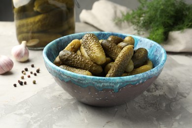 Photo of Pickled cucumbers in bowl on grey textured table, closeup