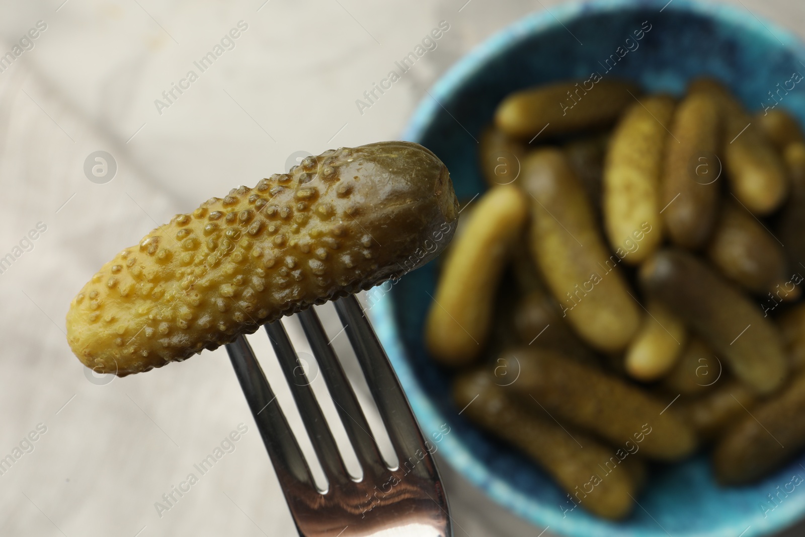 Photo of Fork with pickled cucumber and bowl full of ones on table, top view