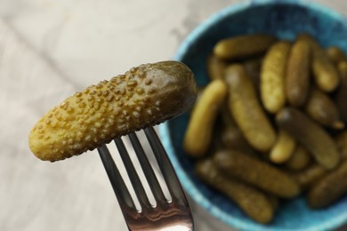 Fork with pickled cucumber and bowl full of ones on table, top view