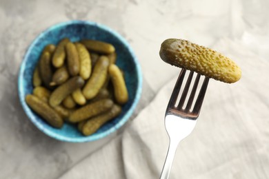 Photo of Fork with pickled cucumber and bowl full of ones on table, top view