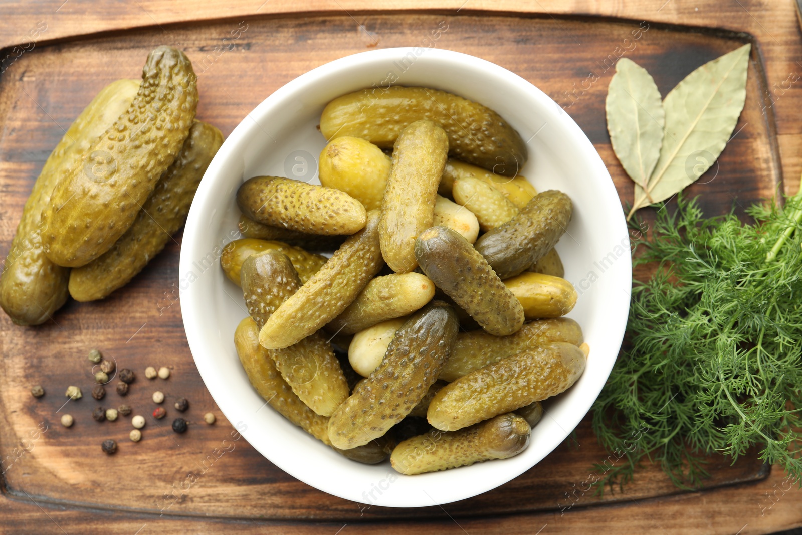 Photo of Pickled cucumbers in bowl, dill and peppercorns on wooden board, flat lay