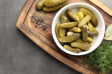 Photo of Pickled cucumbers in bowl, dill and peppercorns on grey textured table, top view