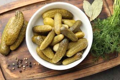 Photo of Pickled cucumbers in bowl, dill and peppercorns on wooden board, top view