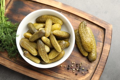 Photo of Pickled cucumbers in bowl, dill and peppercorns on grey table, top view
