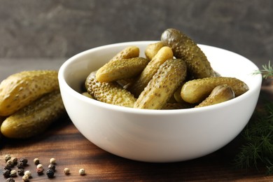 Pickled cucumbers in bowl and peppercorns on wooden board, closeup