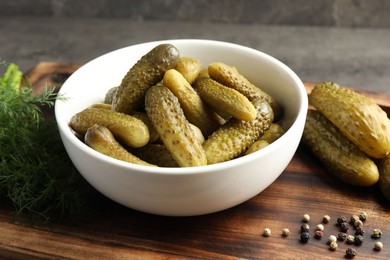 Photo of Pickled cucumbers in bowl, dill and peppercorns on wooden board, closeup