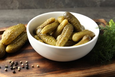 Photo of Pickled cucumbers in bowl, dill and peppercorns on wooden board, closeup