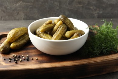 Photo of Pickled cucumbers in bowl, dill and peppercorns on wooden board, closeup