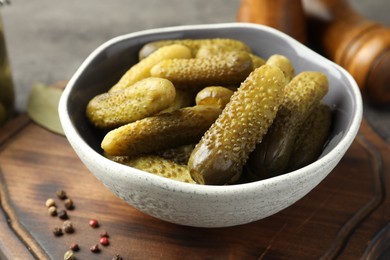 Photo of Pickled cucumbers in bowl and peppercorns on wooden board, closeup