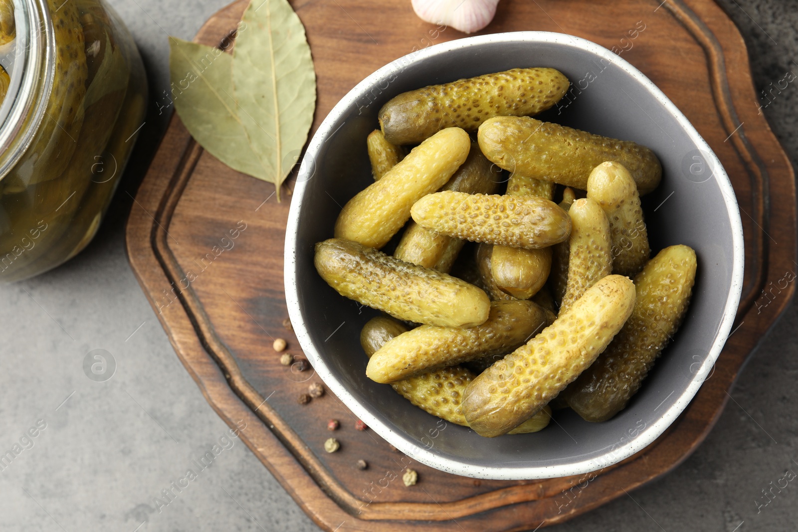 Photo of Pickled cucumbers in bowl and spices on grey textured table, top view
