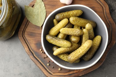 Pickled cucumbers in bowl and spices on grey textured table, top view