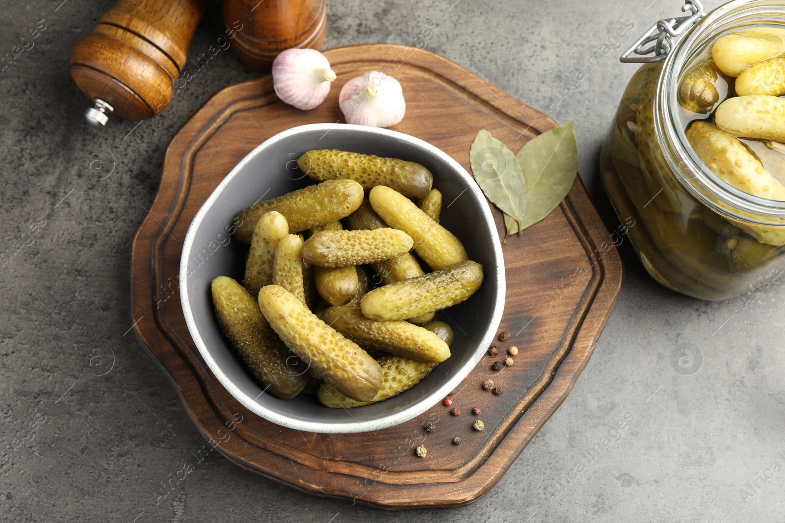 Photo of Pickled cucumbers in bowl, jar and spices on grey textured table, flat lay