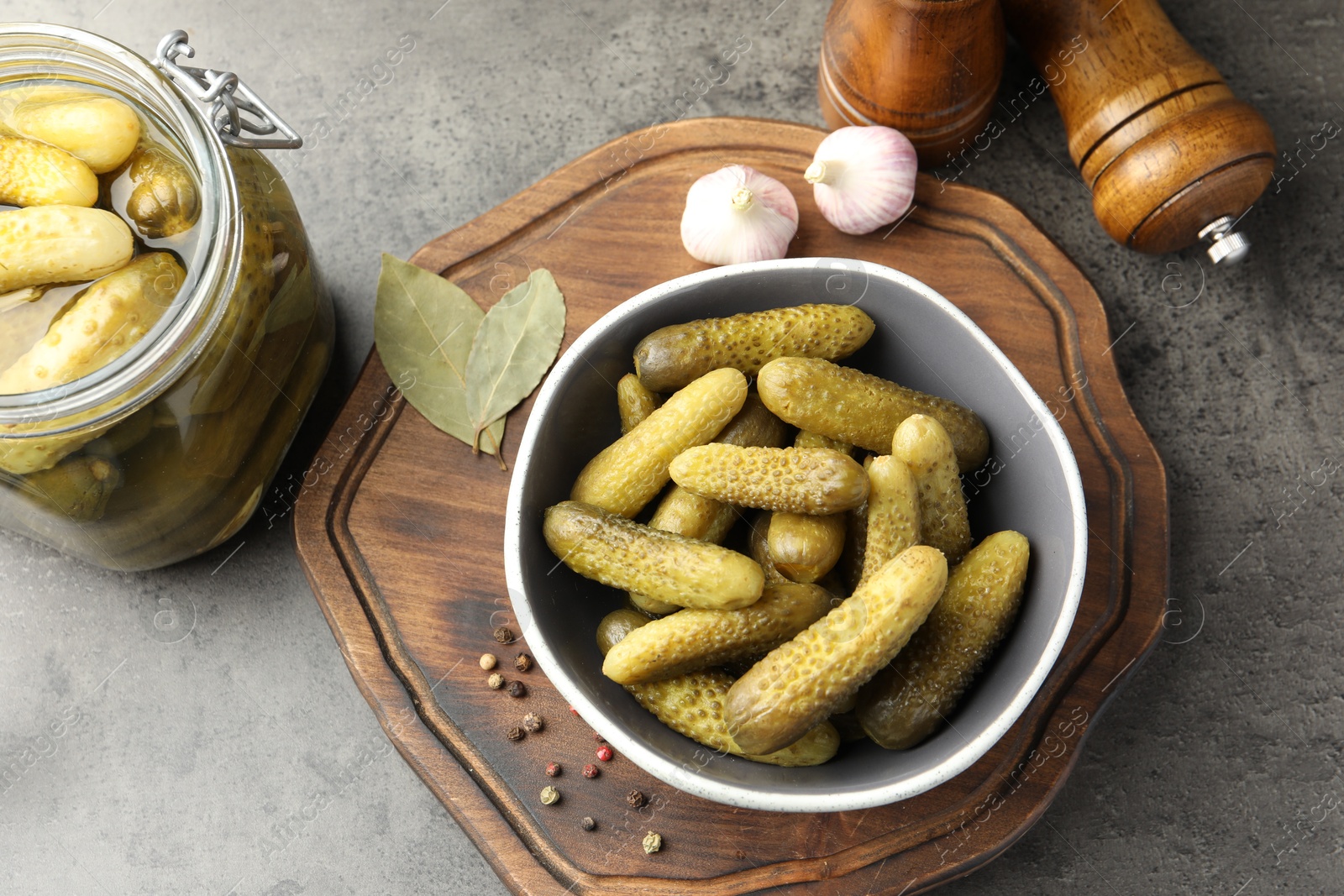 Photo of Pickled cucumbers in bowl, jar and spices on grey textured table, flat lay