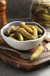 Photo of Pickled cucumbers in bowl, fork and spices on grey table