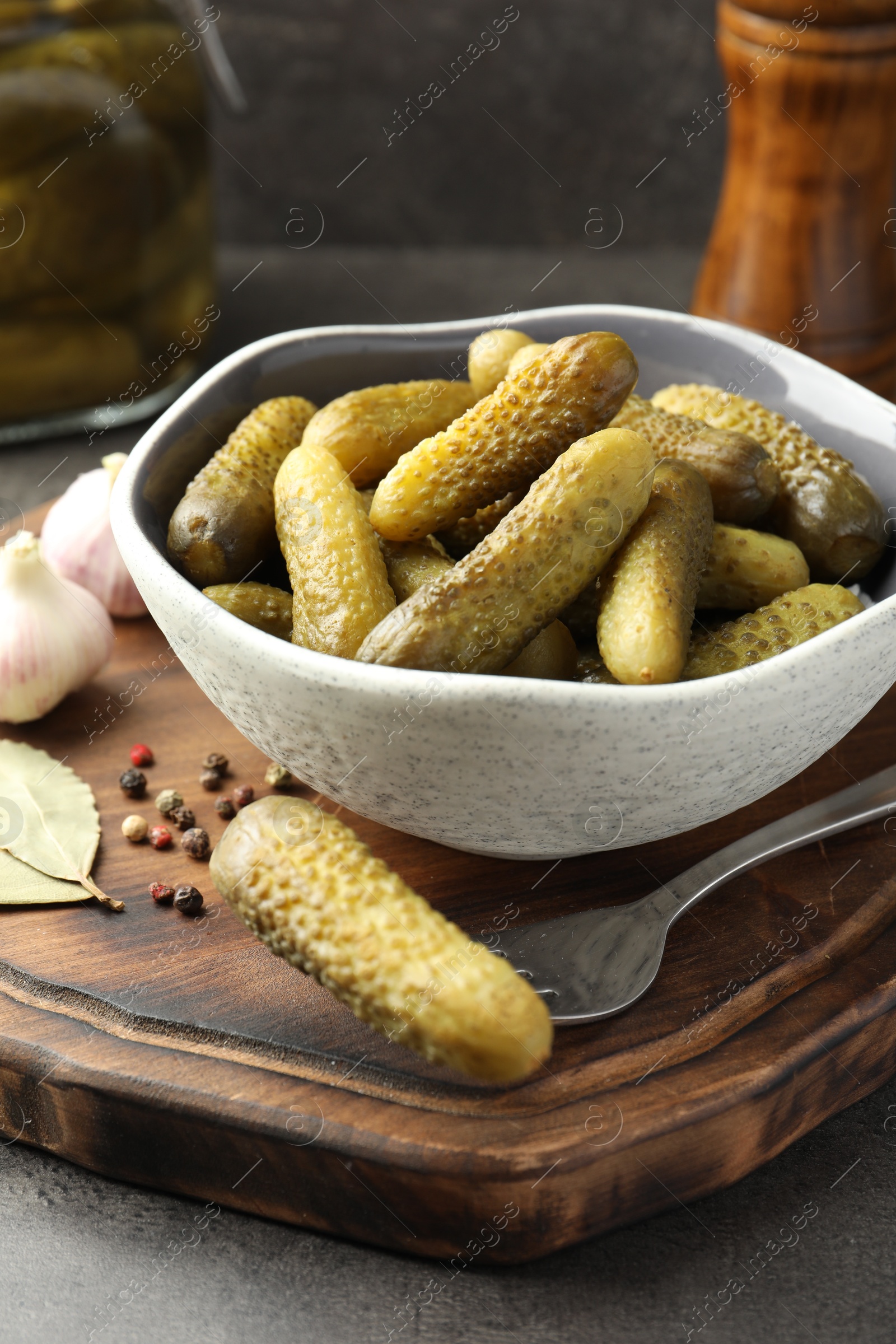 Photo of Pickled cucumbers in bowl, fork and spices on grey table