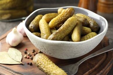 Photo of Pickled cucumbers in bowl, fork, peppercorns, bay leaves and garlic on table, closeup