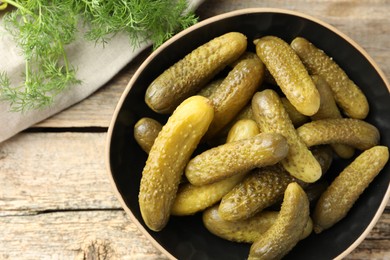 Photo of Pickled cucumbers in bowl and dill on wooden table, top view