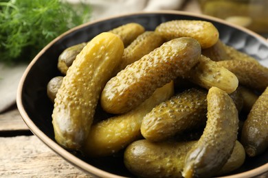 Pickled cucumbers in bowl on wooden table, closeup