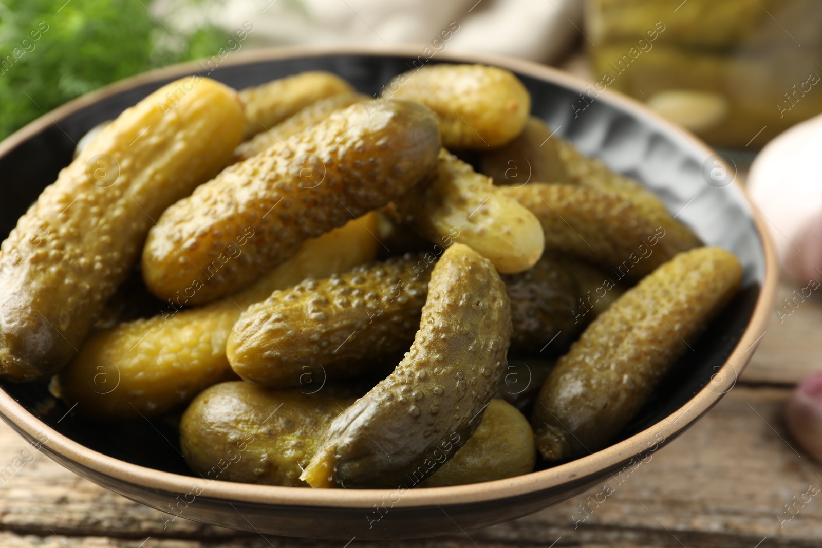 Photo of Pickled cucumbers in bowl on wooden table, closeup