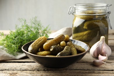 Photo of Pickled cucumbers in bowl, dill and garlic on wooden table