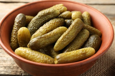 Pickled cucumbers in bowl on wooden table, closeup