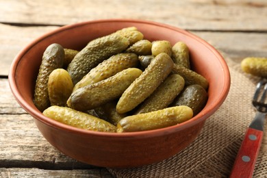 Pickled cucumbers in bowl on wooden table, closeup