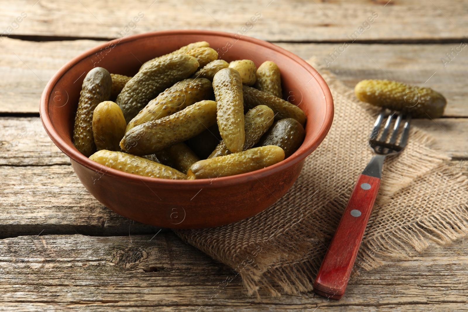 Photo of Pickled cucumbers in bowl and fork on wooden table