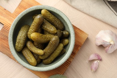 Photo of Pickled cucumbers in bowl and garlic on wooden table, flat lay