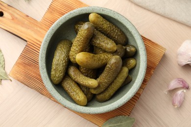 Pickled cucumbers in bowl and garlic on wooden table, flat lay