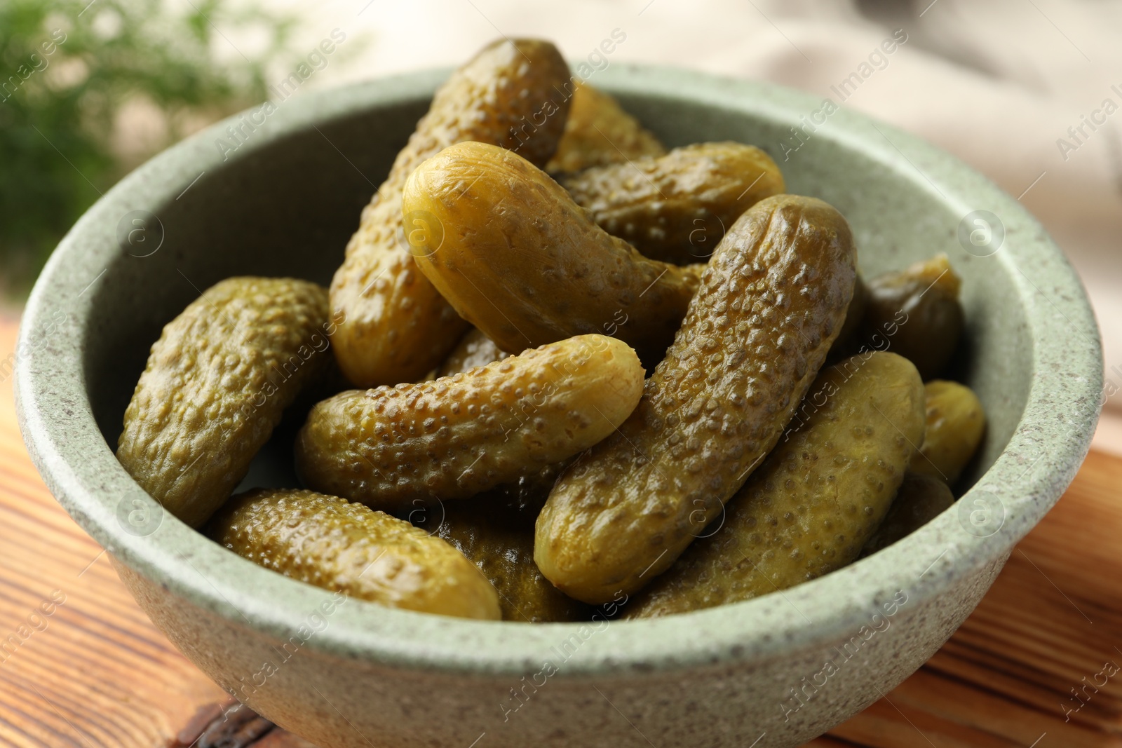 Photo of Pickled cucumbers in bowl on wooden board, closeup