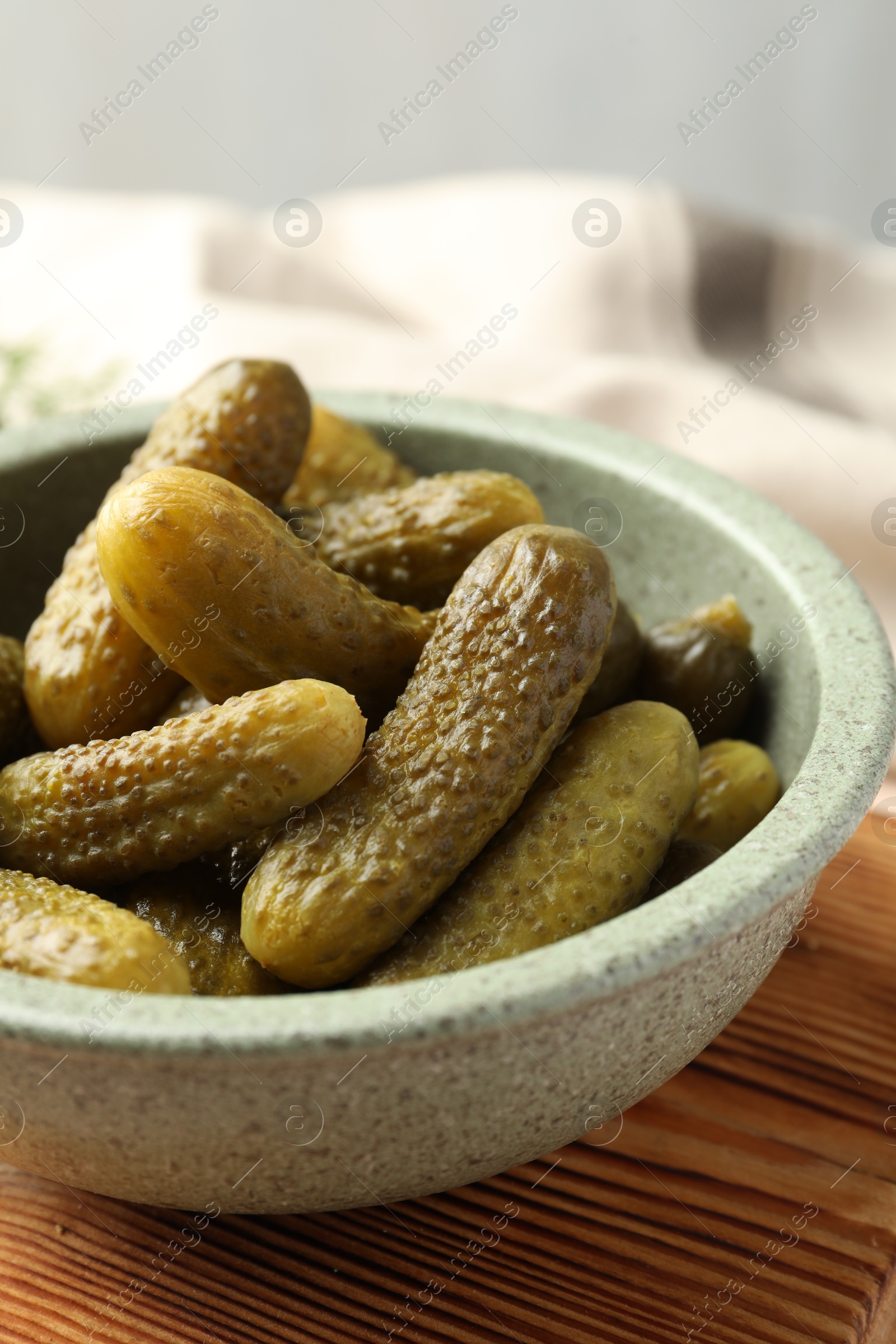 Photo of Pickled cucumbers in bowl on wooden board, closeup