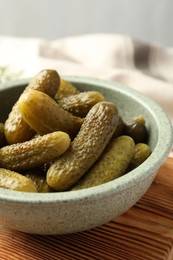 Photo of Pickled cucumbers in bowl on wooden board, closeup