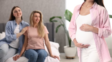 Pregnant surrogate mother and happy lesbian couple at home, selective focus