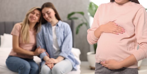 Image of Pregnant surrogate mother and happy lesbian couple at home, selective focus