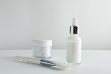 Photo of Bottle of chemical peel liquid, jar and brush on light background. Peeling procedure