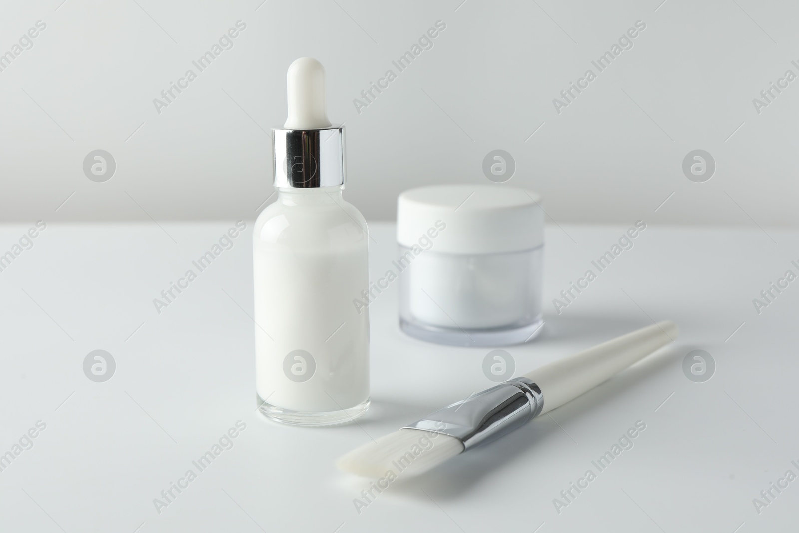 Photo of Bottle of chemical peel liquid, jar and brush on light background. Peeling procedure