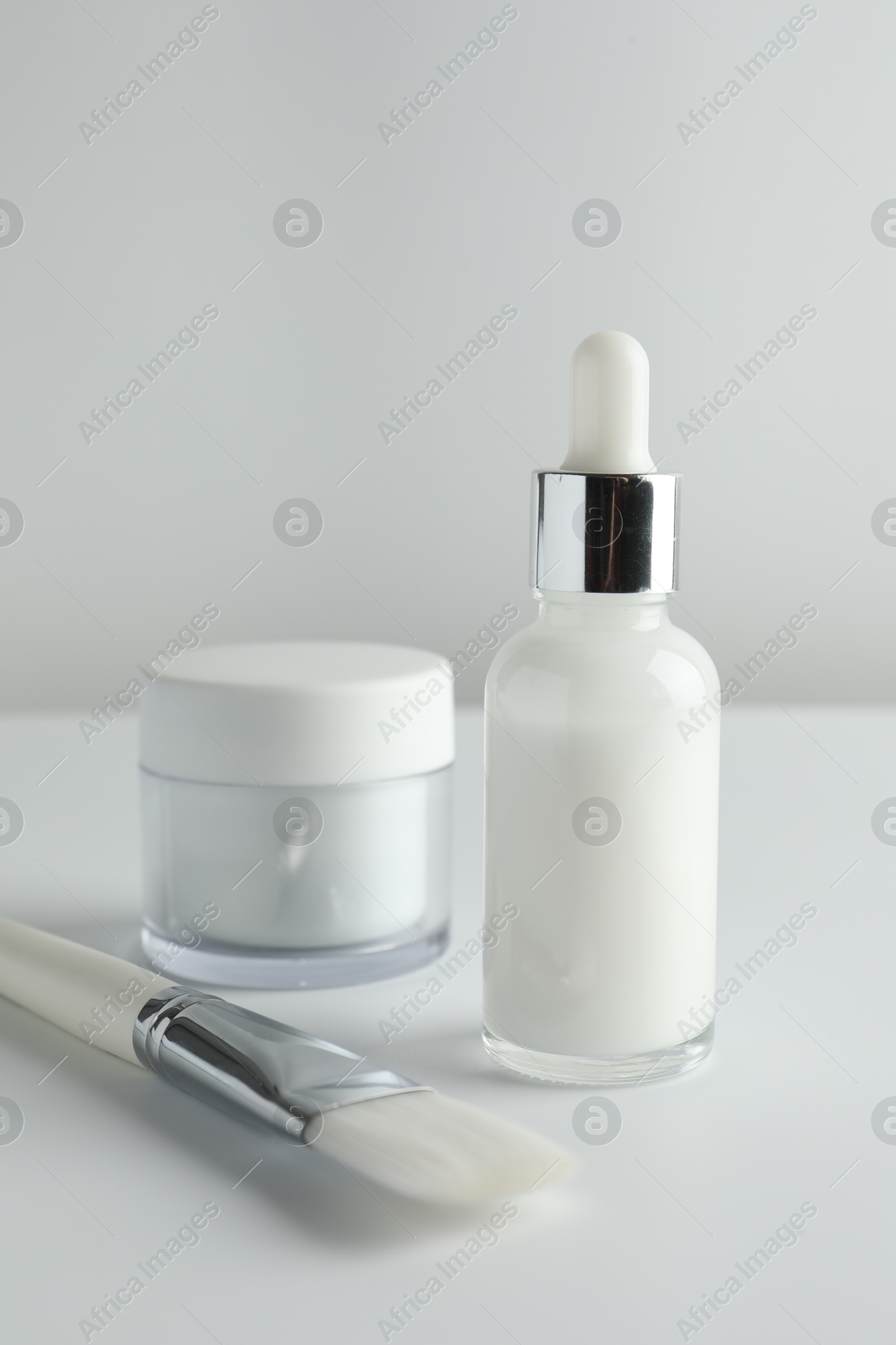 Photo of Bottle of chemical peel liquid, jar and brush on light background. Peeling procedure