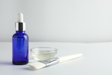 Photo of Bottle of chemical peel, bowl with liquid and brush on light background, space for text. Peeling procedure