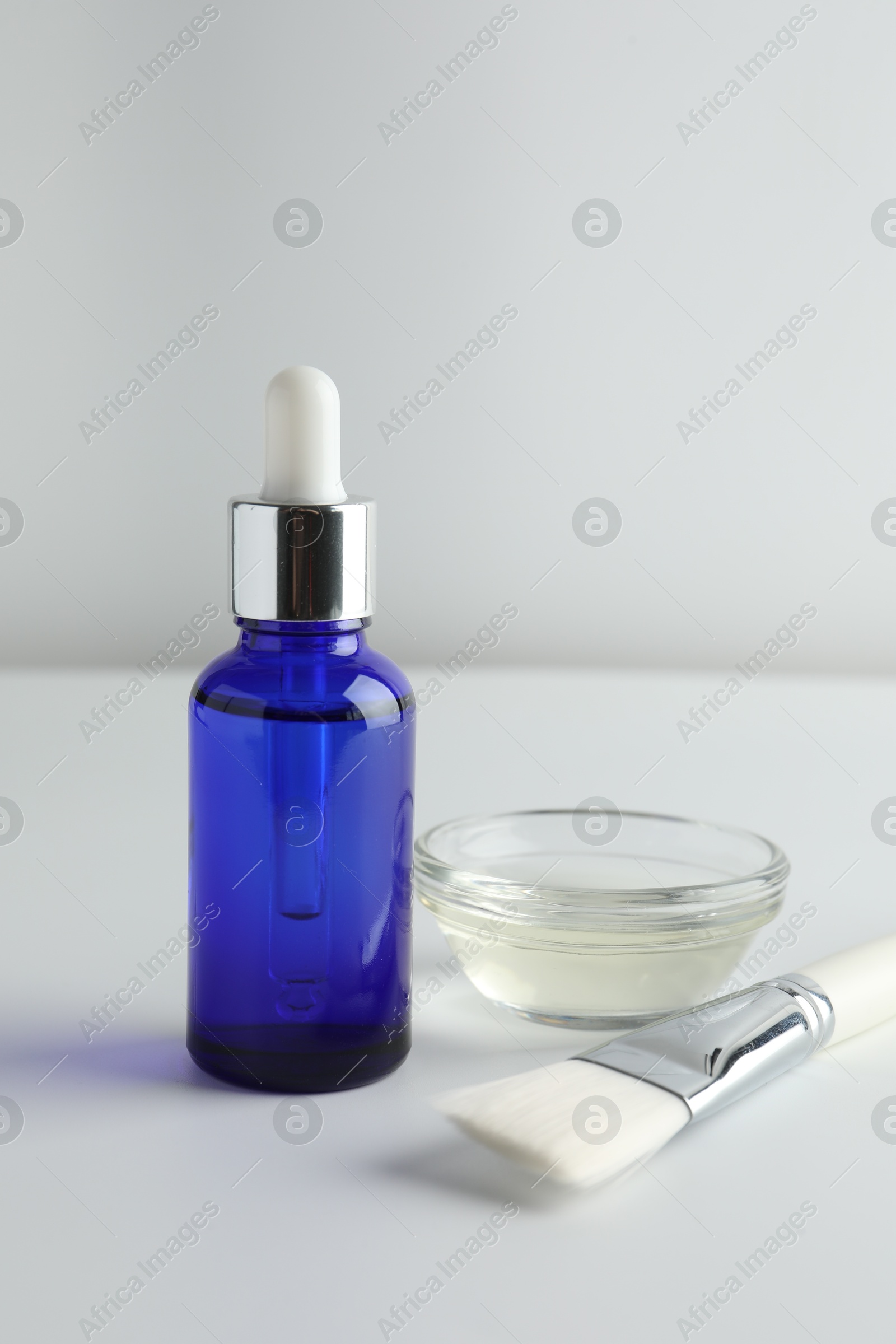 Photo of Bottle of chemical peel, bowl with liquid and brush on light background. Peeling procedure