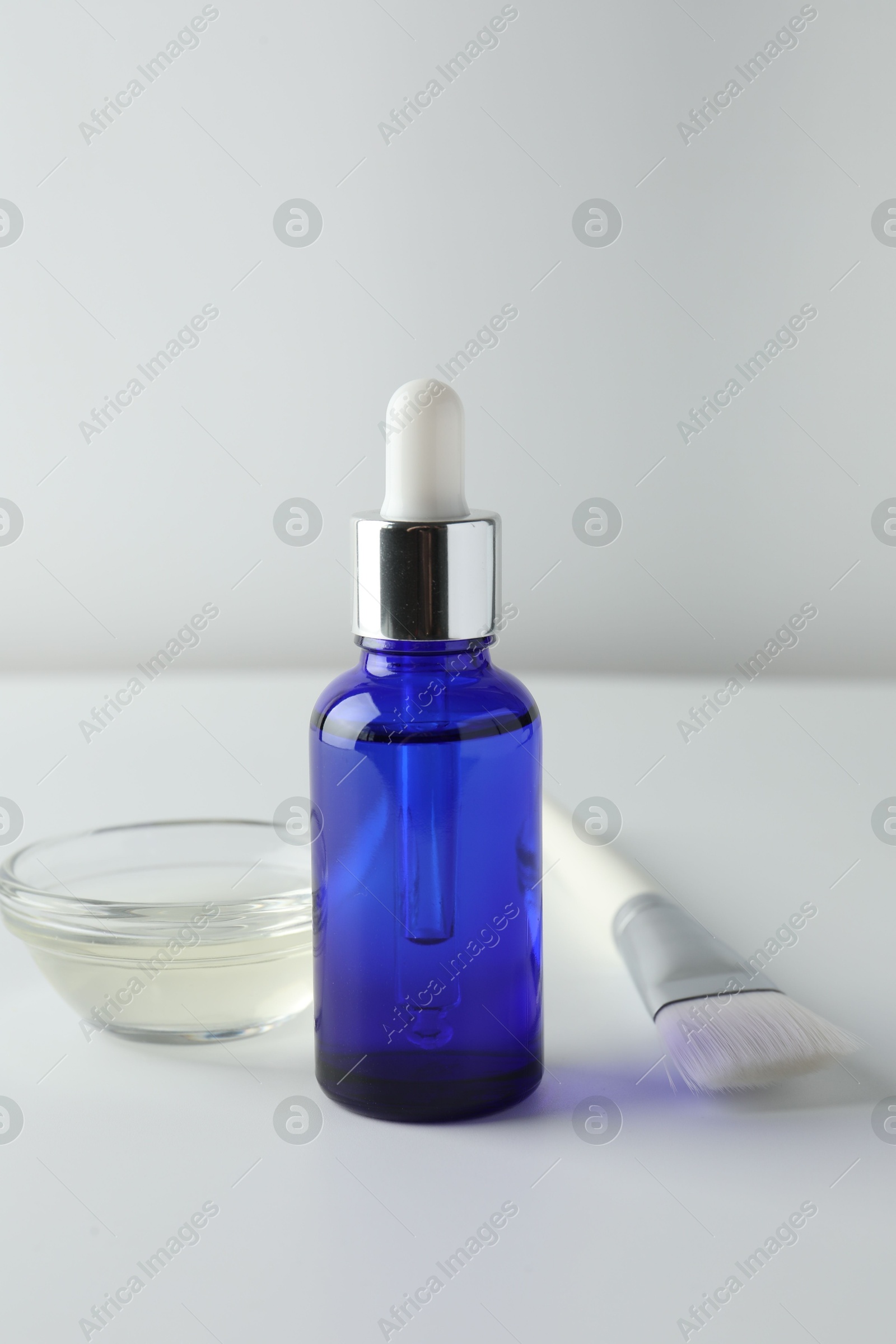 Photo of Bottle of chemical peel, bowl with liquid and brush on light background. Peeling procedure