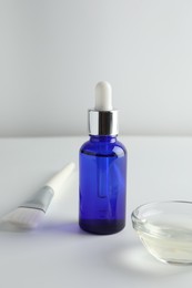 Photo of Bottle of chemical peel, bowl with liquid and brush on light background. Peeling procedure