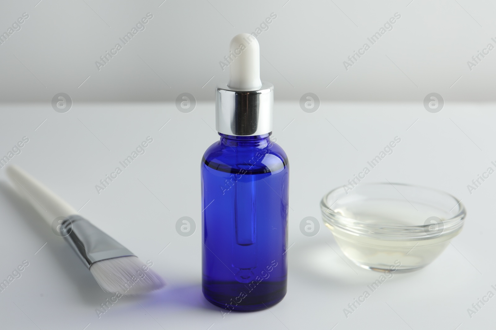 Photo of Bottle of chemical peel, bowl with liquid and brush on light background, closeup. Peeling procedure