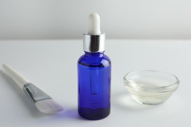 Bottle of chemical peel, bowl with liquid and brush on light background, closeup. Peeling procedure