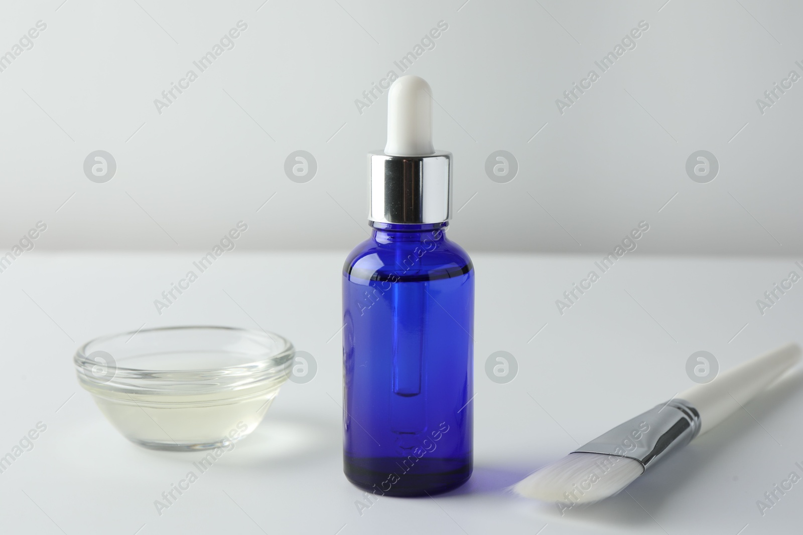 Photo of Bottle of chemical peel, bowl with liquid and brush on light background. Peeling procedure