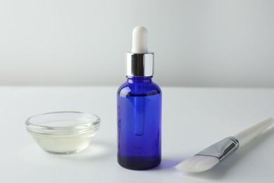 Photo of Bottle of chemical peel, bowl with liquid and brush on light background. Peeling procedure