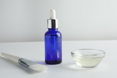 Bottle of chemical peel, bowl with liquid and brush on light background. Peeling procedure