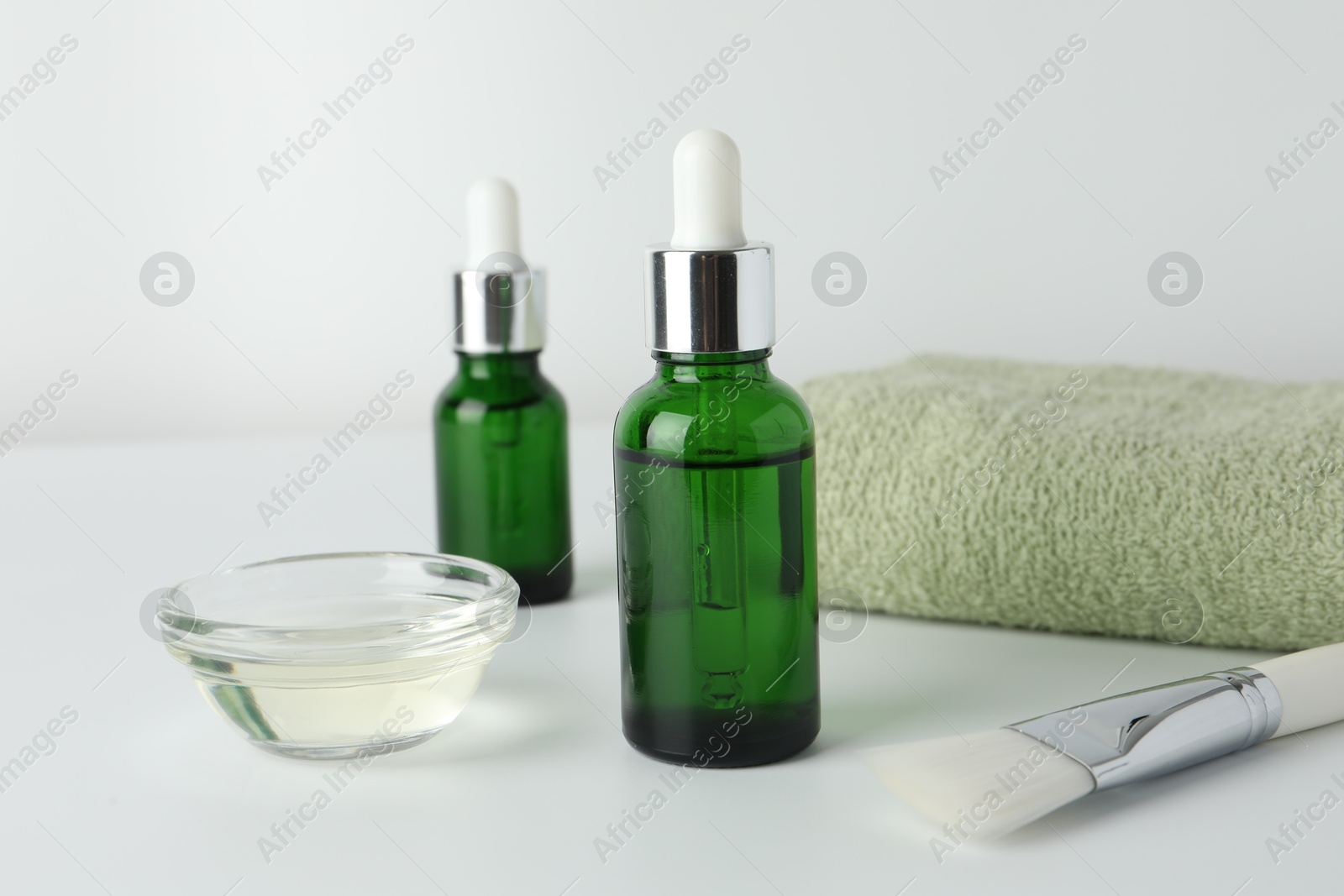 Photo of Bottles of chemical peel, bowl with liquid, towel and brush on light background, closeup. Peeling procedure